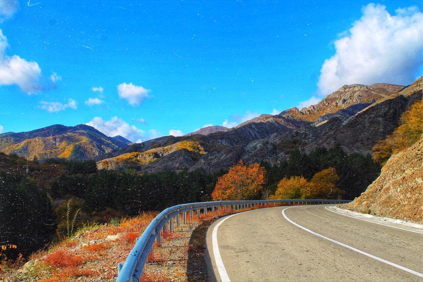 A winding road through the Ateni valley among hills with red and orange autumn trees