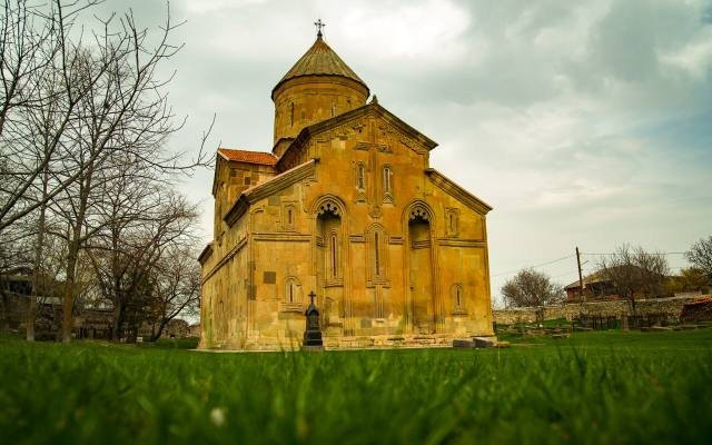 The golden stone Ertatsminda Cathedral with its tall dome, seen across a lawn