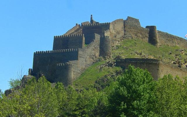 The stone walls and towers of Gori Fortress climbing a rocky green hill