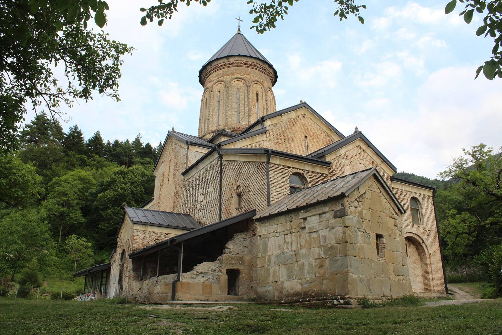 The brick and stone church of Kintsvisi Monastery with its tall drum and dome, among trees