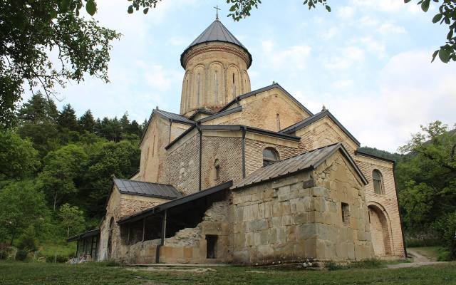 The brick and stone church of Kintsvisi Monastery with its tall drum and dome, among trees