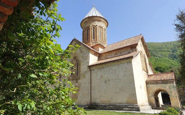 The domed church of Kvatakhevi Monastery behind a stone gate, among green trees