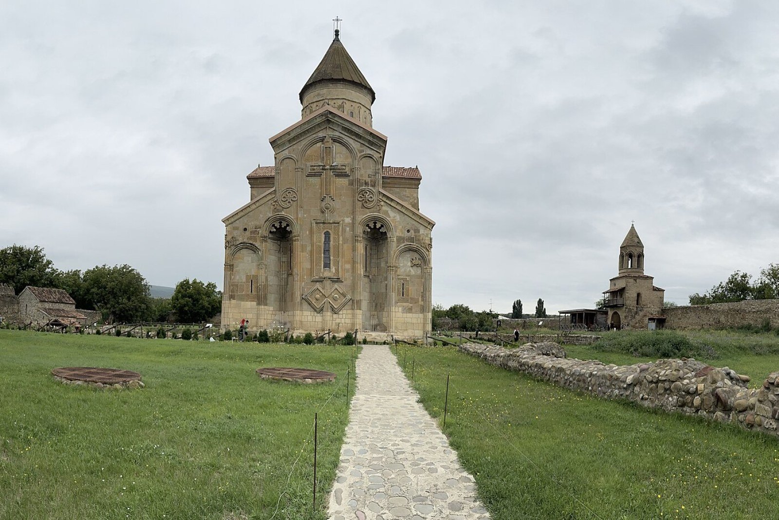 The east façade of Samtavisi Cathedral, with its carved cross and arches, at the end of a stone path