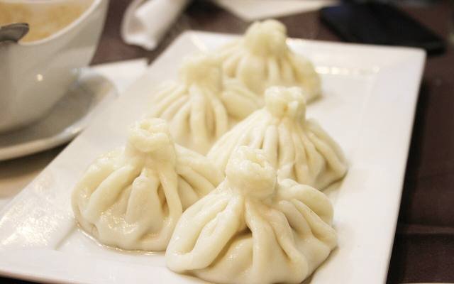 Five khinkali dumplings on a white plate beside a cup of coffee
