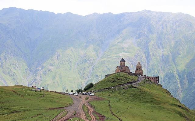 Gergeti Trinity Church on a green hill below the mountains of Kazbegi